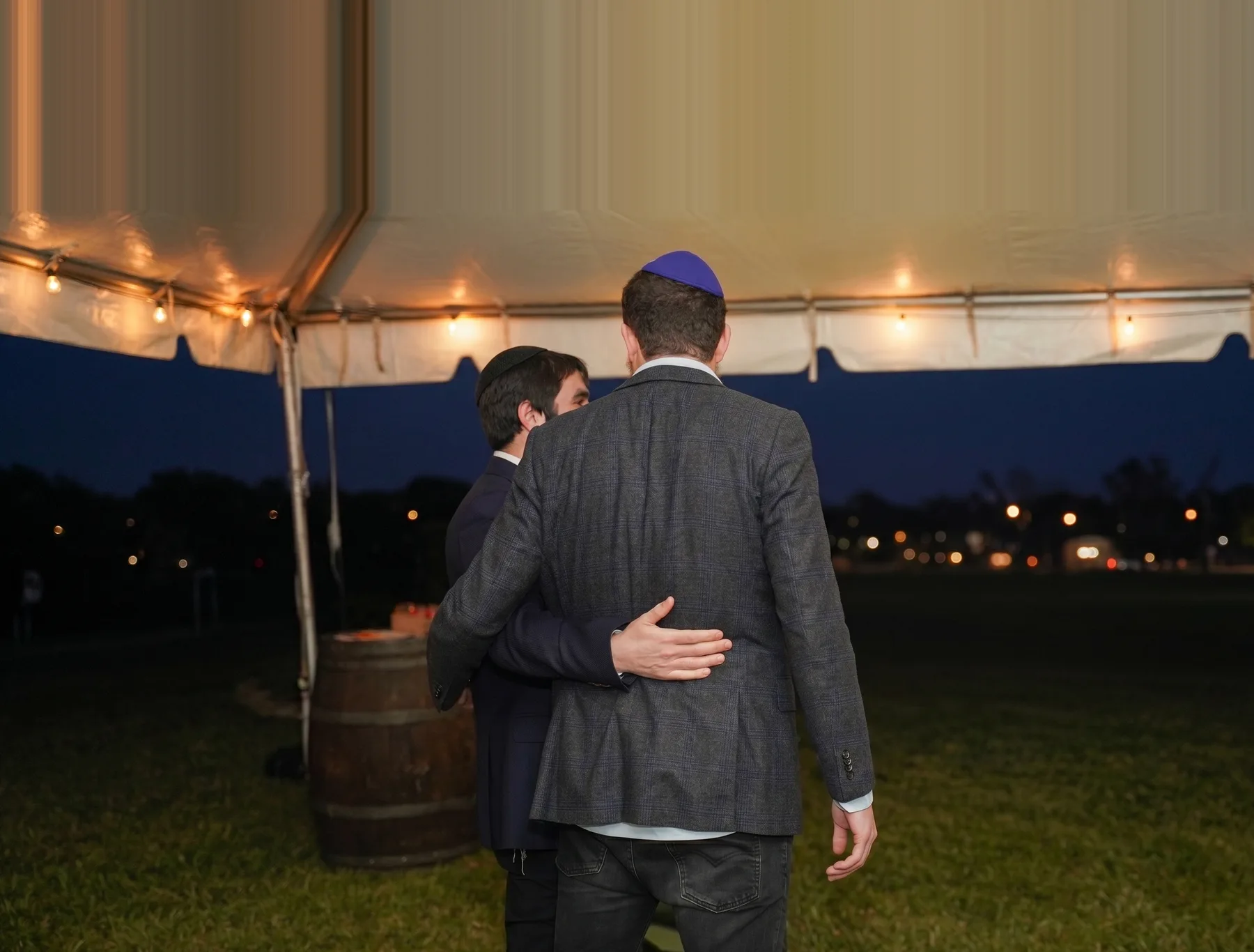 A counselor with his arm around a younger man at an evening gathering