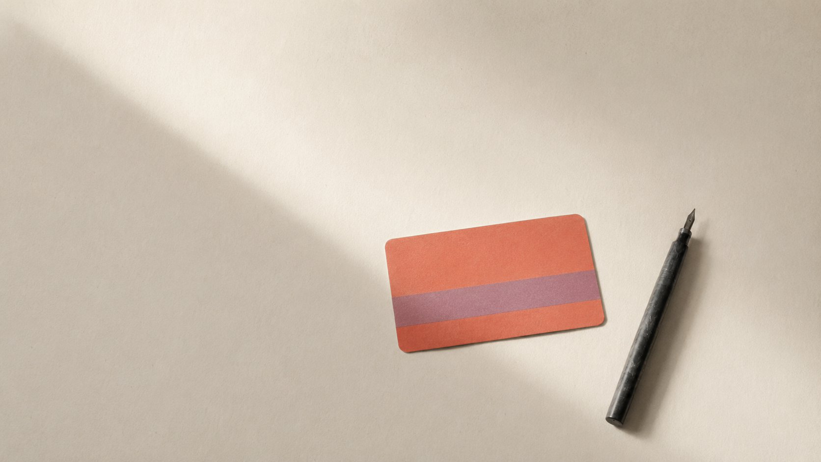 A coral credit card and a pen on a cream desk
